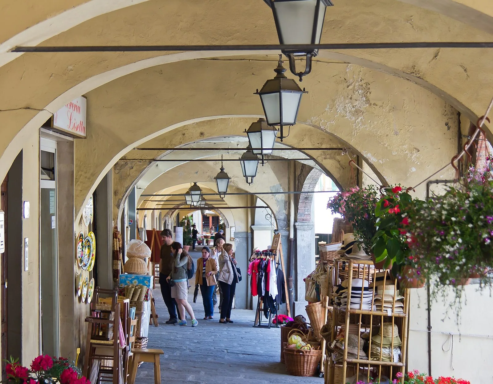 I portici ad archi di Piazza Matteotti a Greve in Chianti con lanterne appese, cesti di vimini, cappelli di paglia e ceramiche esposte