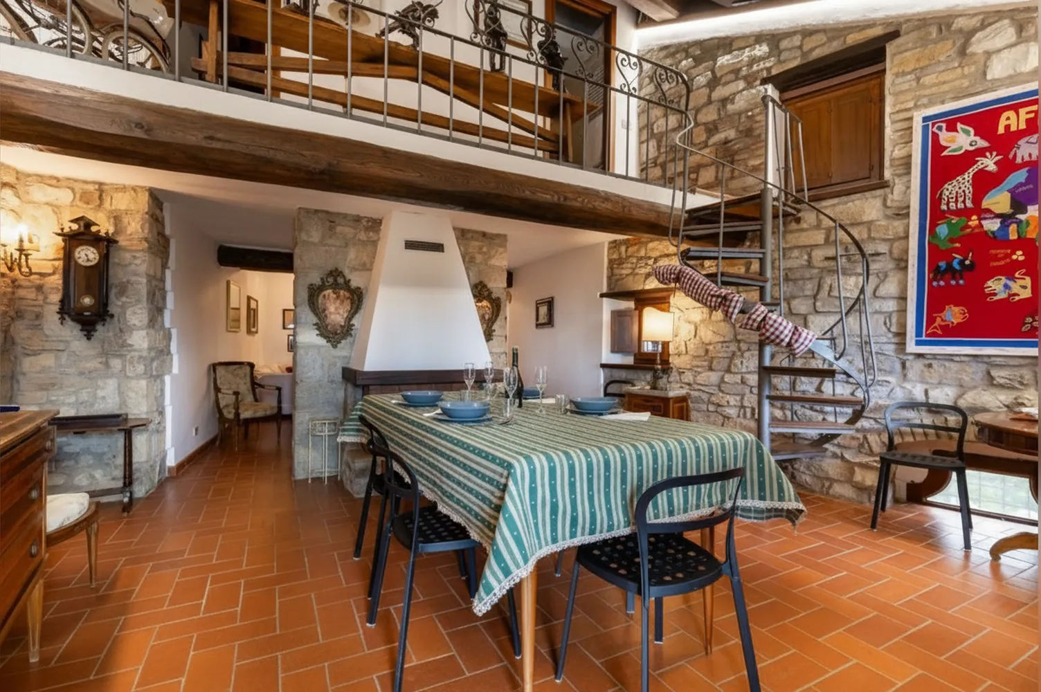 La sala da pranzo con il tavolo apparecchiato, la scala a chiocciola e il soppalco in legno