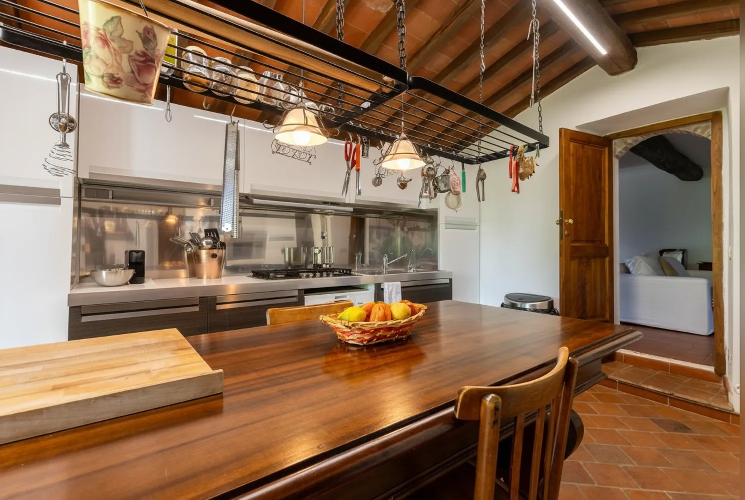 La cucina con il bancone in legno, le pentole appese e la porta verso il soggiorno